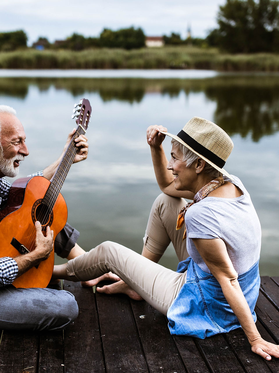 Older couple playing guitar on a lakeside dock